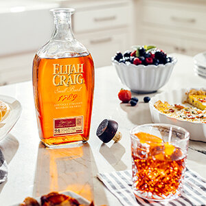 Elijah Craig small batch sitting on a kicthen counter with the sun shining through the bottle, Right, Boulevardier in rocks glass.