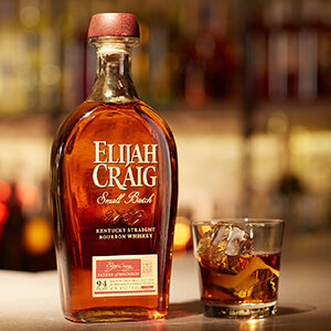 Left, Elijah Craig bottle sitting on bar top with bourbon in a rocks glass to the right
